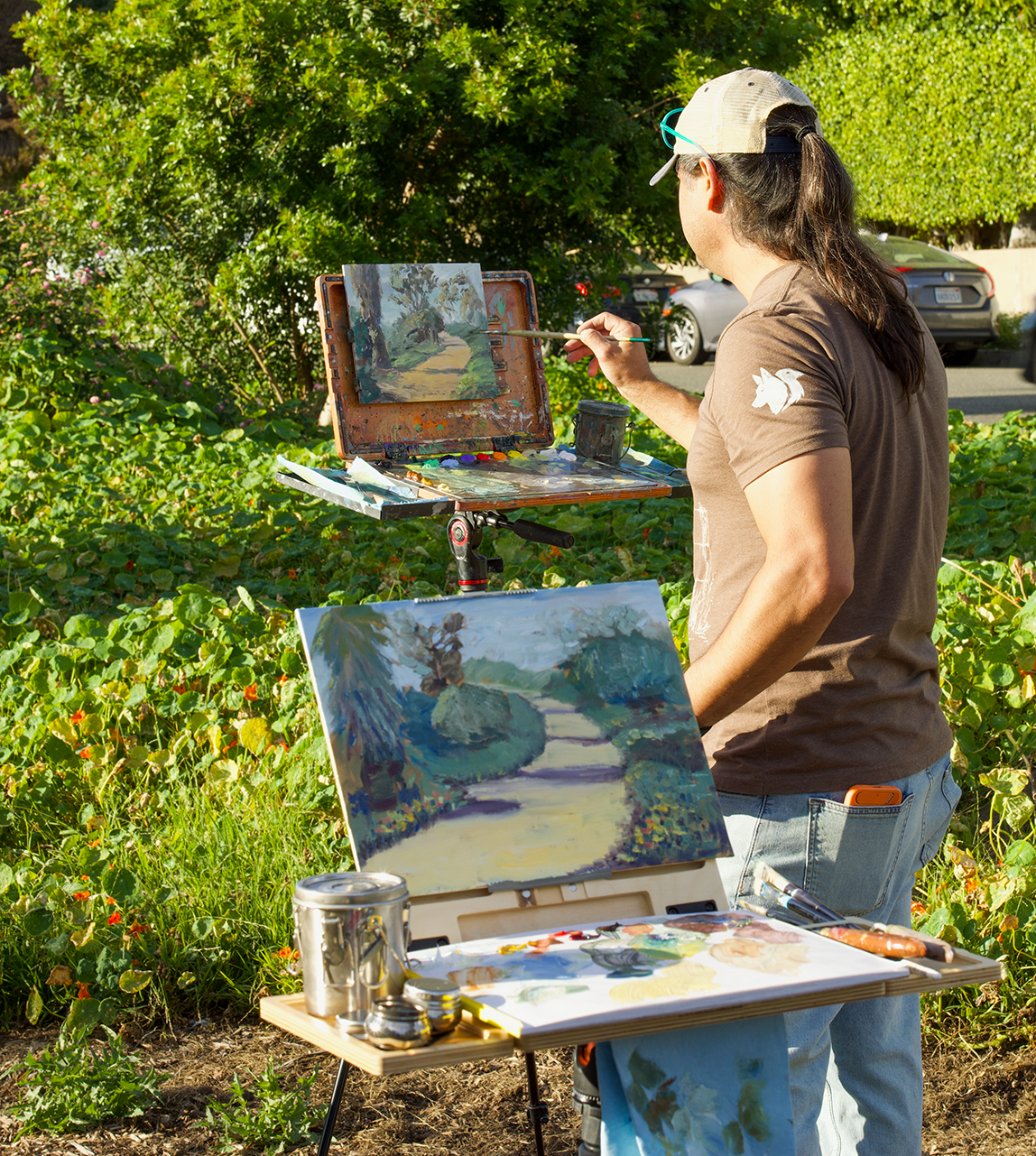 Person painting outdoors with a landscape scene in a garden setting