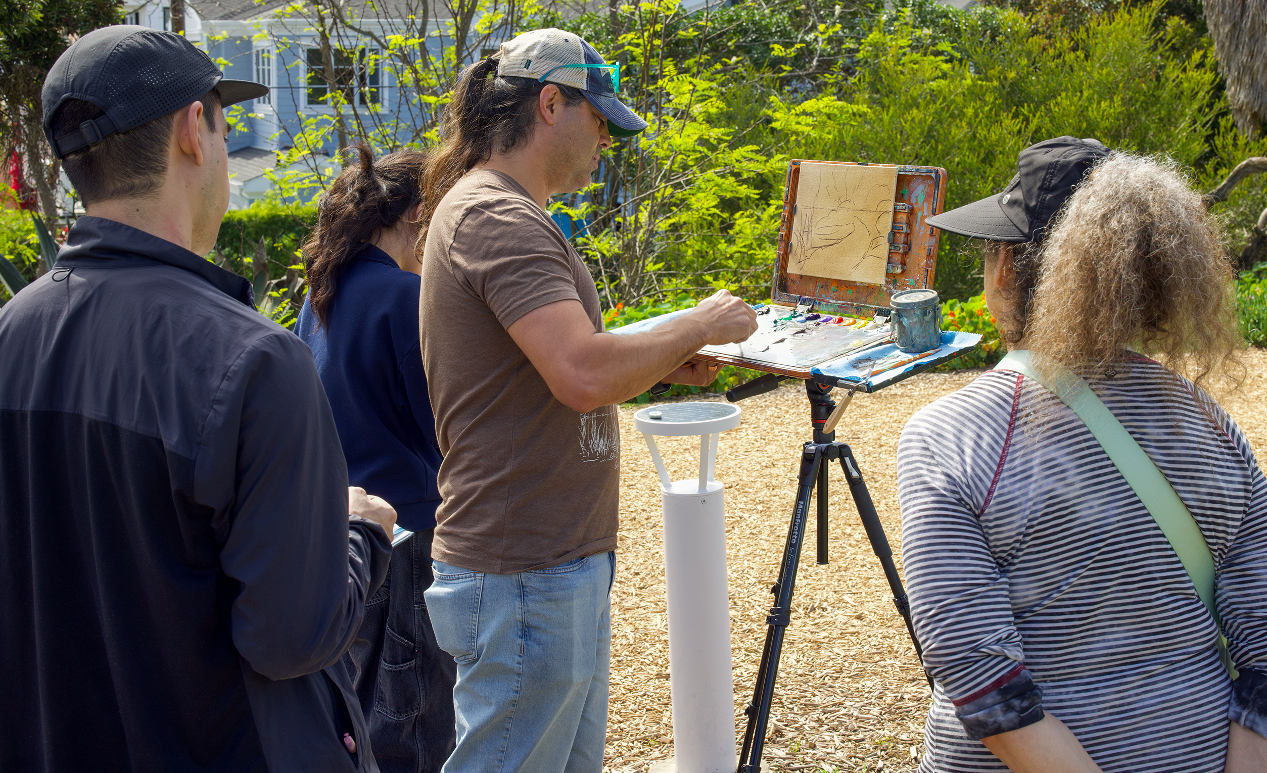 Artist painting outdoors with a group of people observing